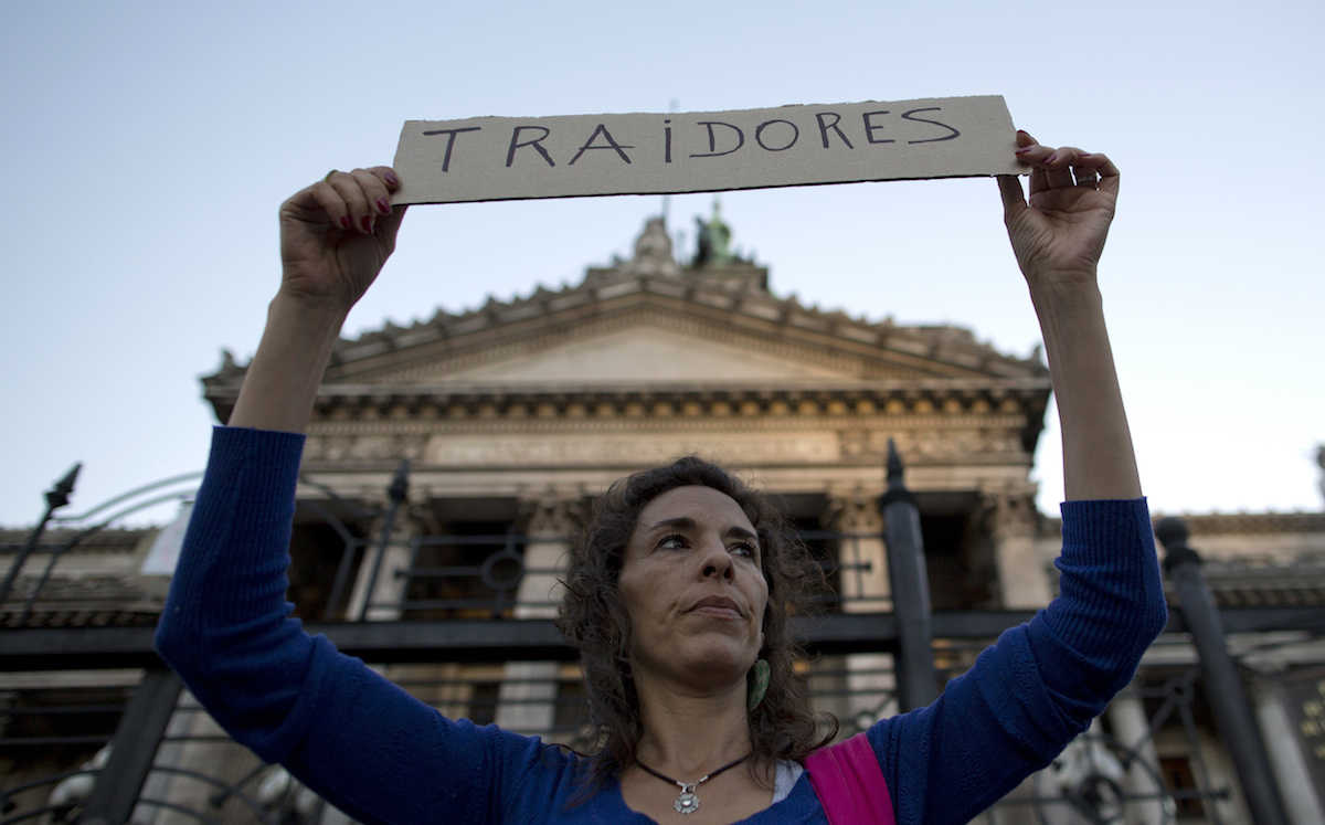 A demonstrator holds a sign that says in Spanish: "Traitors" outside Congress, directed at lawmakers who are debating a new debt payment deal with U.S. creditors in Buenos Aires, Argentina, Wednesday, March 30, 2016. Under the deal, if passed, Argentina would pay to resolve all related claims, including those from a group led by hedge fund manager Paul Singer's group in New York. (AP Photo/Natacha Pisarenko)